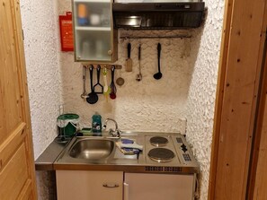 A compact kitchen with a sink, stove, and various utensils hanging on the wall. - Family room - Pferde- und Schafhof Klinser (Vordertambergau)