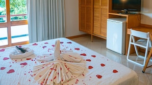 A hotel room with a bed, a TV, a small fridge, and a desk. - Porto das Naus Praia Hotel (Porto Seguro)