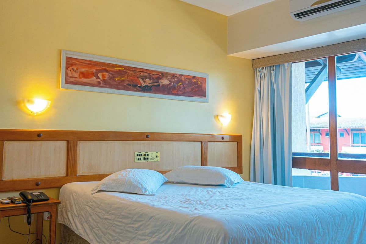 Una habitación de hotel con cama, mesita de noche, lámpara y un cuadro en la pared.