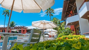 A poolside area with lounge chairs and umbrellas, surrounded by palm trees and a clear blue sky. - Porto das Naus Praia Hotel (Porto Seguro)