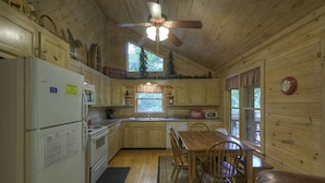 Een keuken in cottage-stijl met houten kastjes, een koelkast, kookplaat en een eettafel met stoelen.