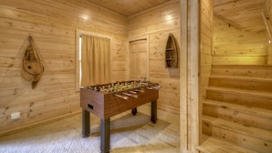 Een kamer met houten vloer, een tafelvoetbalspel, een trap en een raam met gordijnen.