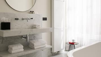 A modern bathroom with a marble sink, a large mirror, a bathtub, and a glass table with a cup.