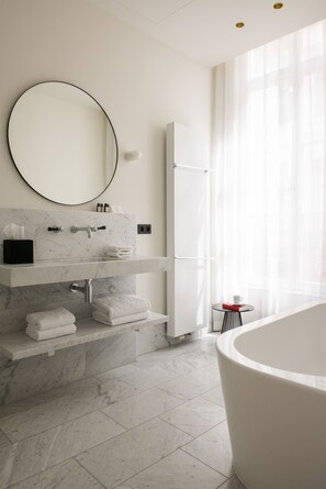 A modern bathroom with a marble sink, a large mirror, a bathtub, and a glass table with a cup.