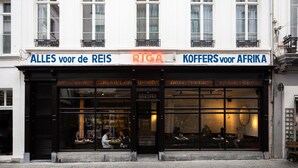 A building with a storefront featuring signs in multiple languages, including "ALLES voor de Reis," "RIGA," and "KOFFERS voor Afrika." - Riga Suites Antwerp (Antwerp)