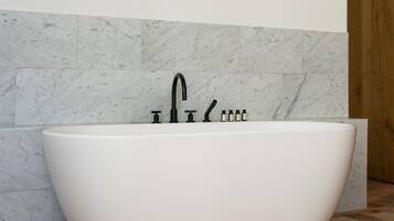 Un baño moderno con una bañera independiente, baldosas de mármol y una puerta de madera.
