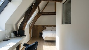 A bedroom with a sloped ceiling, a bed, a desk with a chair, and a window. - Riga Suites Antwerp (Antwerp)
