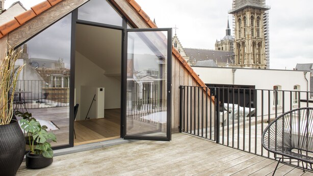 A modern apartment with a large sliding glass door, a wooden deck, and a view of a historic building. - Riga Suites Antwerp (Antwerp)