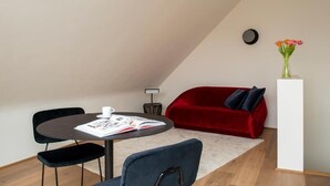 A modern living space with a dining table, two chairs, a red sofa, and a small side table with a vase of flowers. - Riga Suites Antwerp (Antwerp)