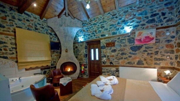 A stone-walled room with a fireplace, a bed with towels, a bathtub, and a wooden ceiling. - Guesthouse Elati - Pella (Edessa)