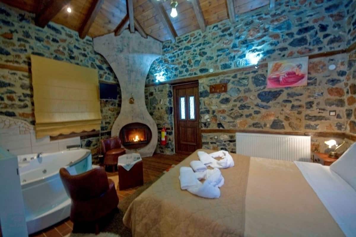 A stone-walled room with a fireplace, a bed with towels, a bathtub, and a wooden ceiling.
