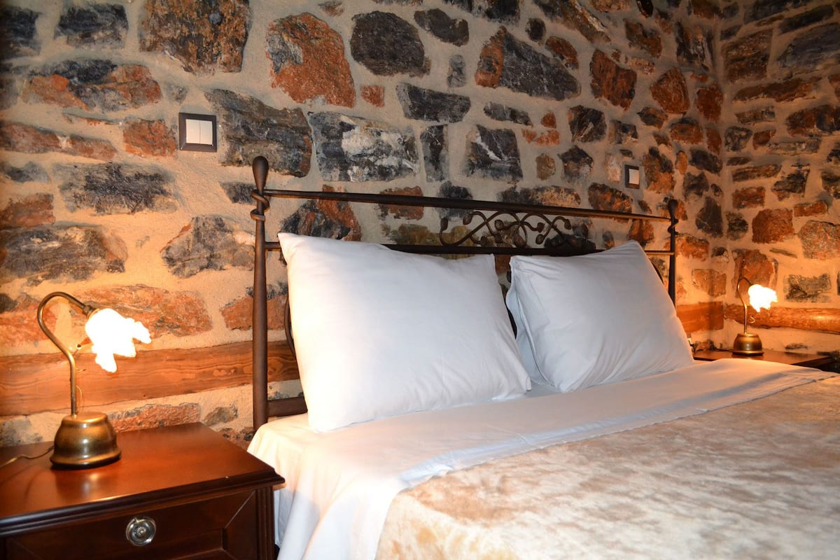 A bed with white linens in a room with a stone wall.