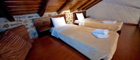 Un dormitorio acogedor en el ático con dos camas, vigas de madera y una pared de piedra.