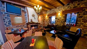A cozy interior with a stone wall, a fireplace, striped chairs, a wooden table, and a television mounted on the wall. - Guesthouse Elati - Pella (Edessa)
