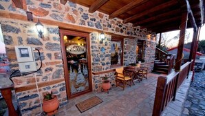A stone building with a wooden entrance, outdoor seating, and a staircase leading to a covered area. - Guesthouse Elati - Pella (Edessa)
