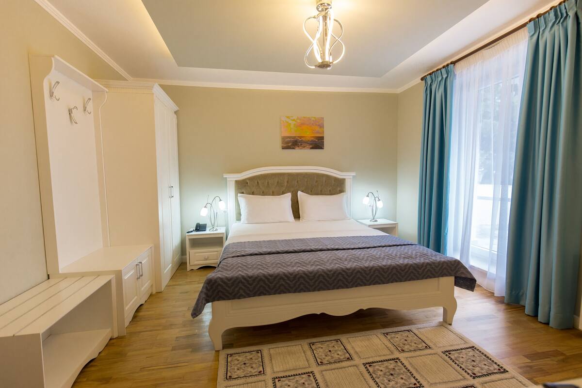 Une chambre à coucher comprenant un lit, des tables de chevet, une commode, une armoire et une fenêtre avec des rideaux.