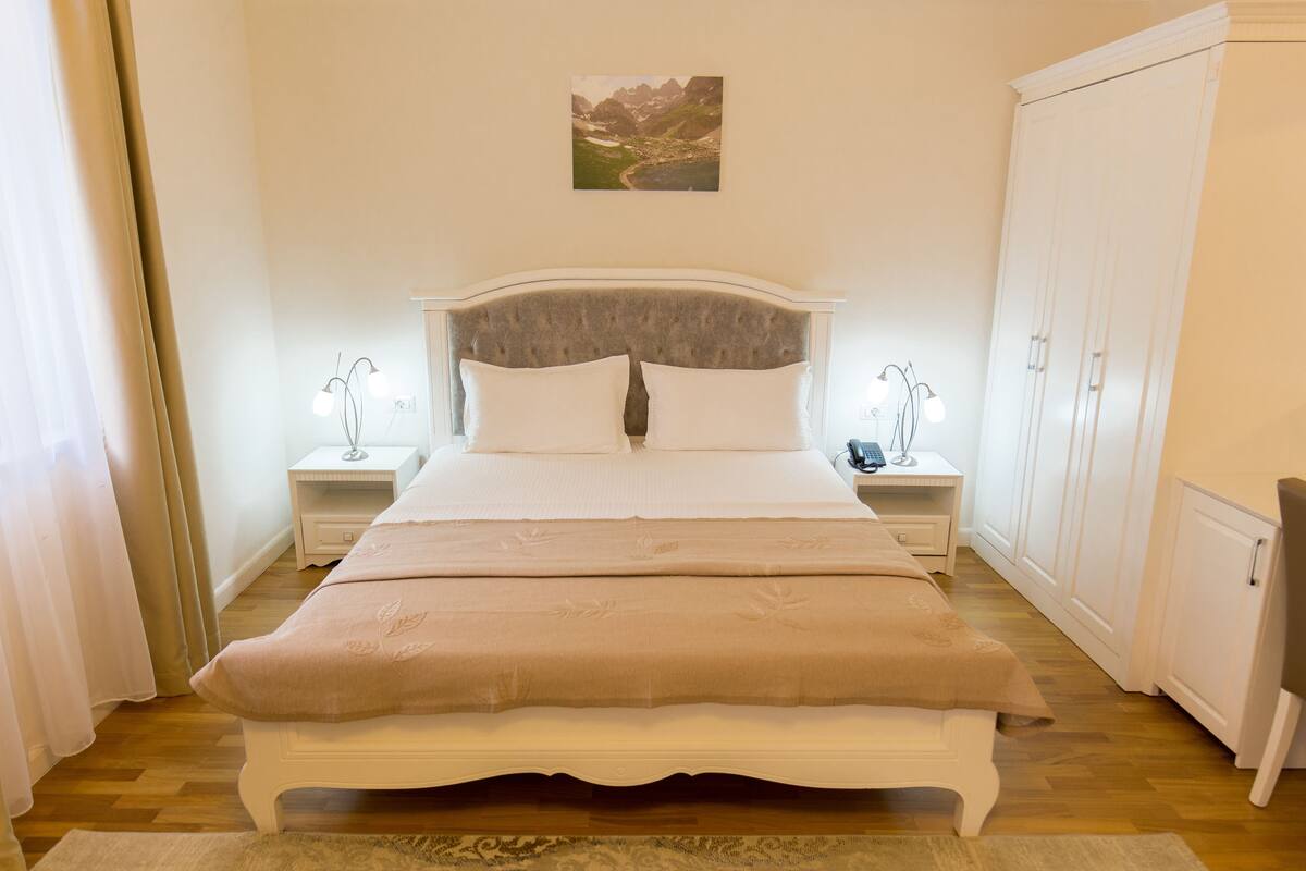 Une chambre à coucher bien rangée, avec un lit, des tables de chevet, une armoire et un tableau accroché au mur.