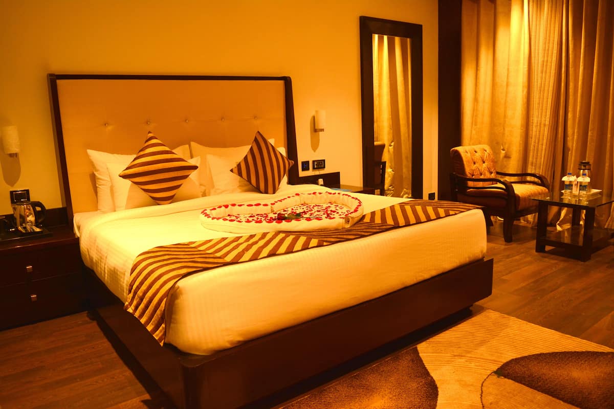 Habitación de hotel con una cama grande, una mesita de noche con lámpara, una silla y una pequeña mesa con botellas.