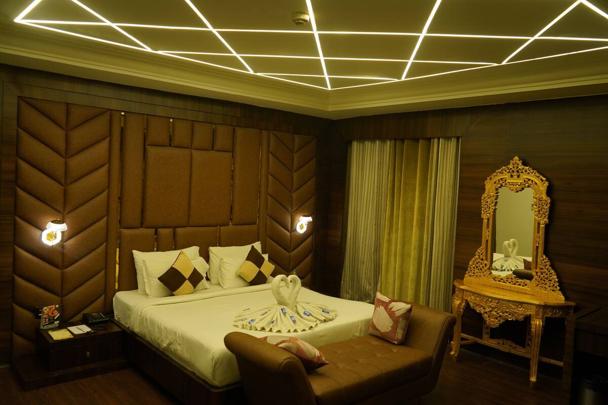 Habitación de hotel con una cama grande, cabecera con diseños geométricos, espejo con detalles ornamentados y un sillón de cuero marrón.