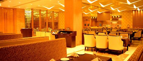 A restaurant with a modern interior, featuring a long dining area with multiple tables and chairs, a patterned wall, and a decorative ceiling design.