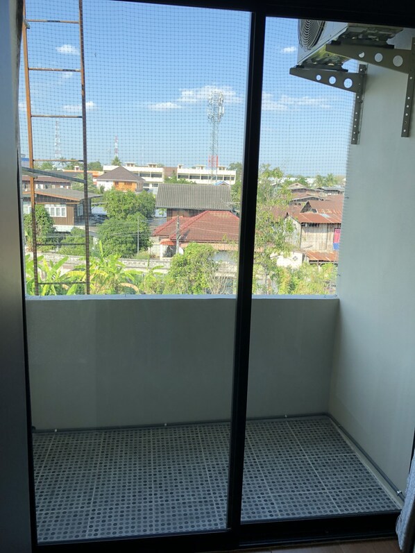 A balcony with a mesh screen, a metal grate floor, and a view of residential buildings.