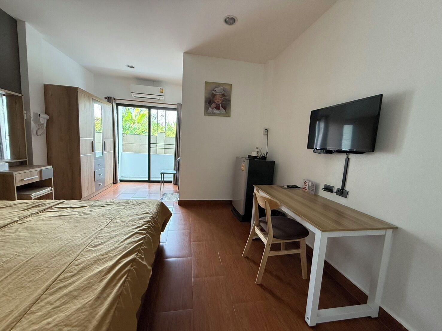 A hotel room with a bed, a desk, a chair, a television, and a sliding door leading to a balcony.