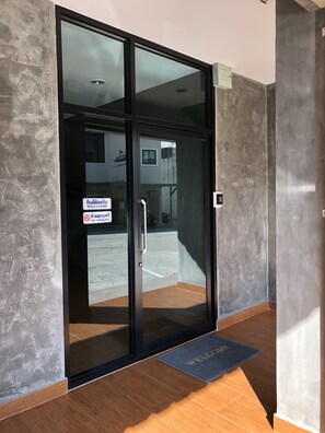A modern entrance with a glass door, a welcome mat, and a no smoking sign.