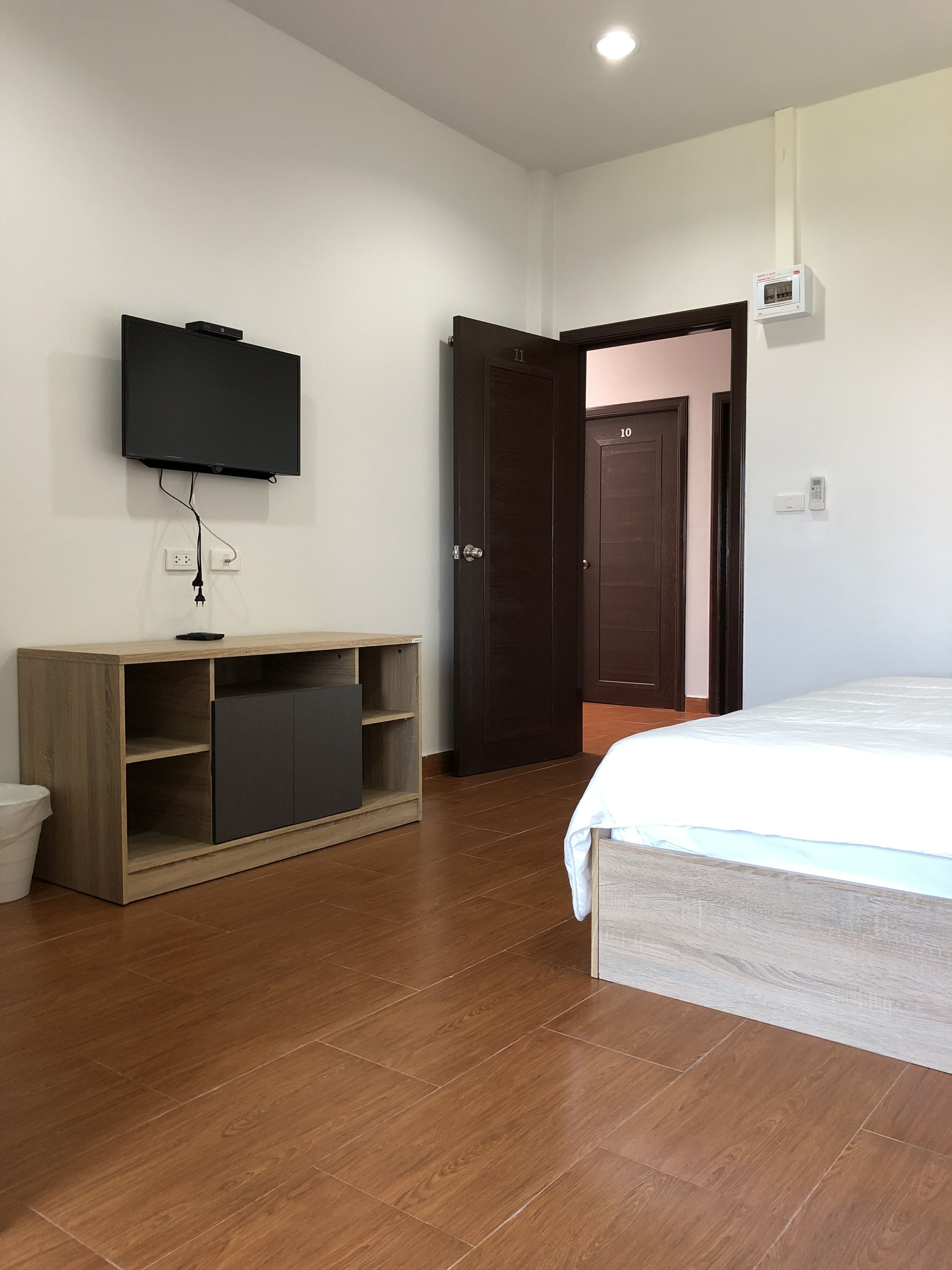 A bedroom with a bed, a TV mounted on the wall, a wooden cabinet, and a door leading to another room.