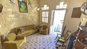 A living room with a stone wall, patterned floor tiles, a sofa, chairs, and a wooden cabinet. - Gaviota B&B (Havana)