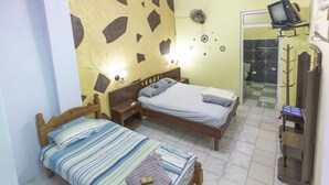 A bedroom with two beds, a wooden headboard, a nightstand, a wall-mounted TV, and a bathroom visible through an open door. - Gaviota B&B (Havana)