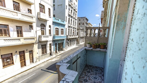 A narrow street with buildings on either side, featuring balconies with potted plants and a tiled floor. - Gaviota B&B (Havana)