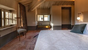 Un dormitorio con una cama grande, una silla de madera, un banco y una ventana con vistas.