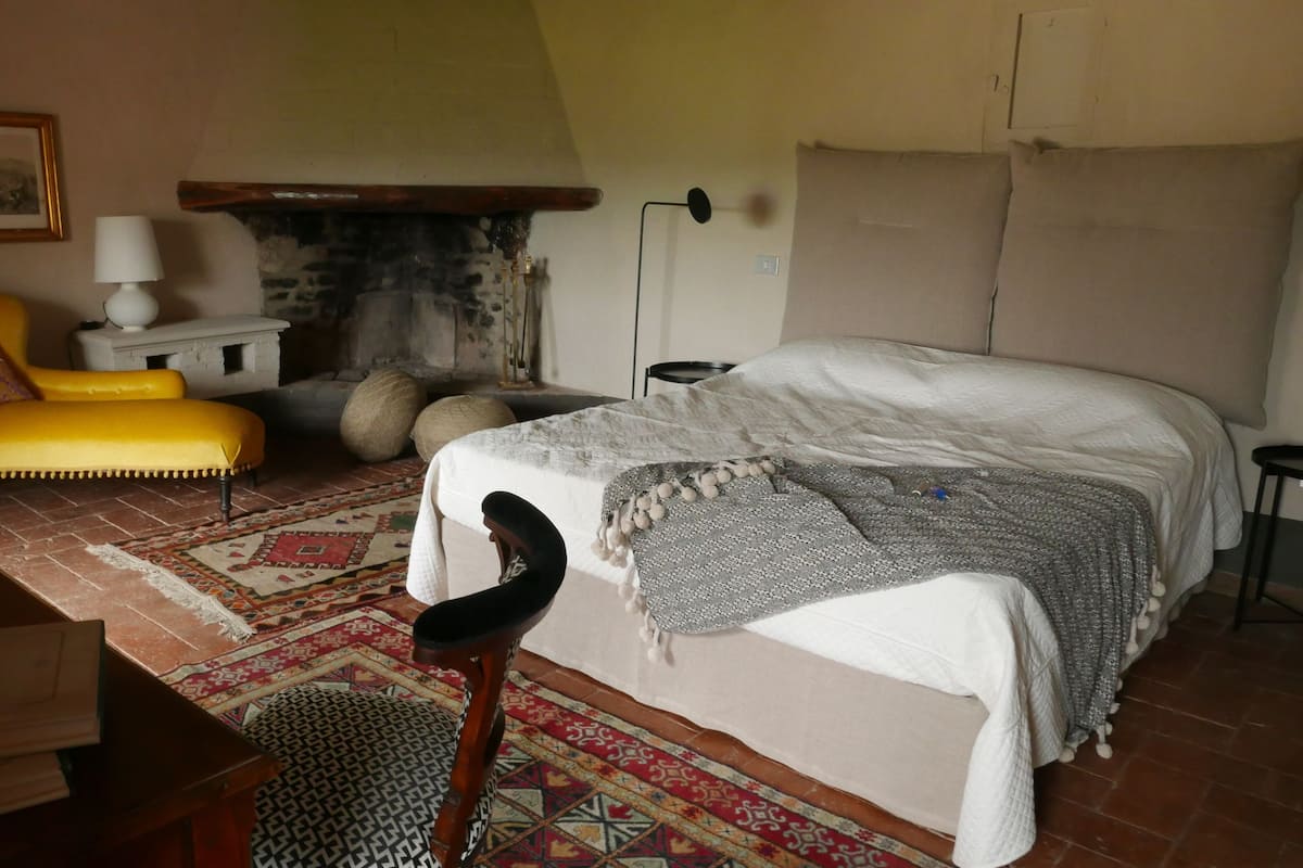 A cozy bedroom with a bed, a yellow armchair, a fireplace, and a patterned rug.