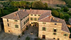 Un gran edificio de piedra histórico con un patio interior, rodeado de abundante vegetación y colinas ondulantes.