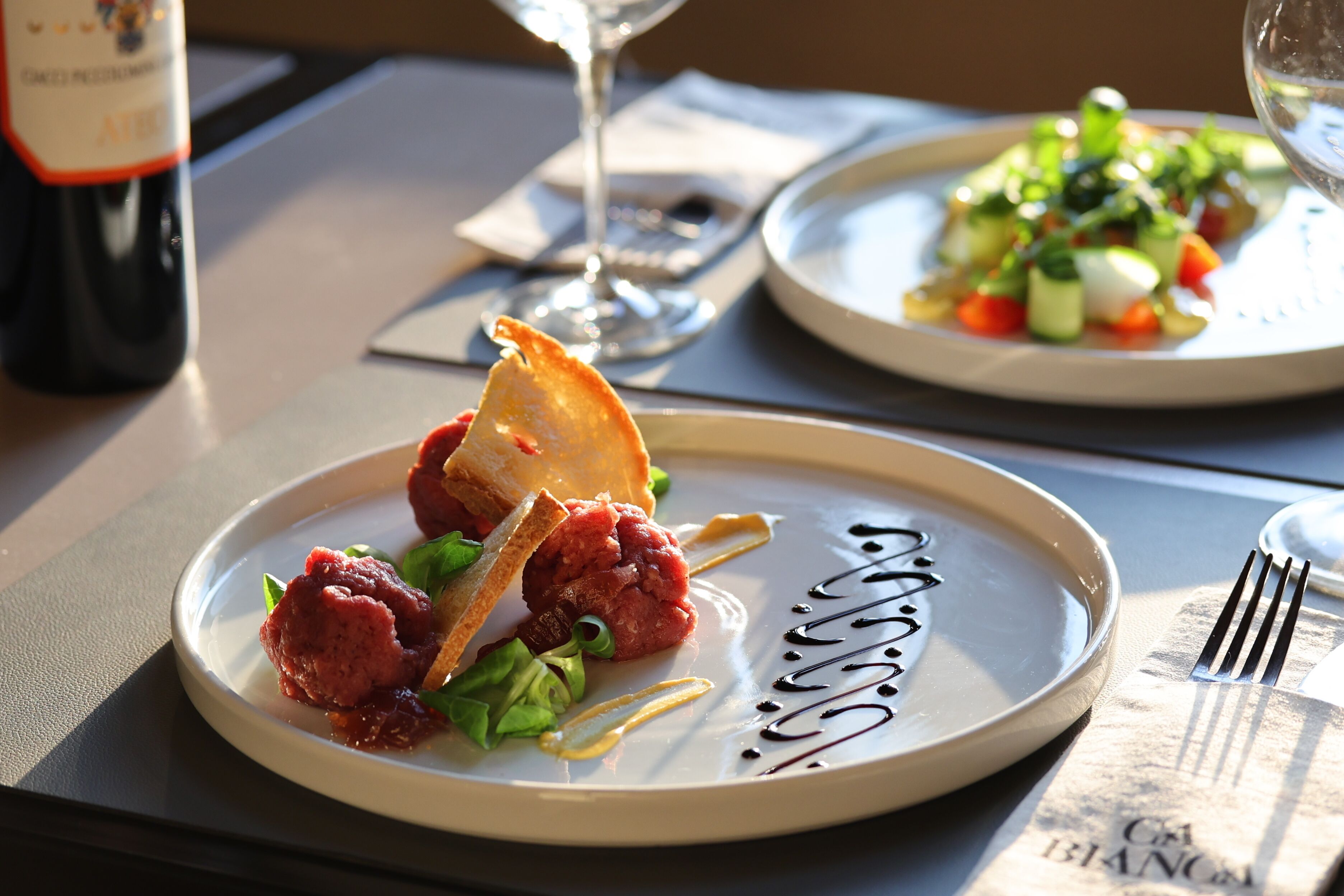 A dining table with plates of food, a wine bottle, and a glass of wine.