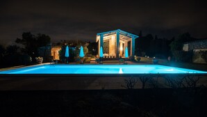 Una piscina con una estructura de quiosco, rodeada de mobiliario exterior y sombrillas.