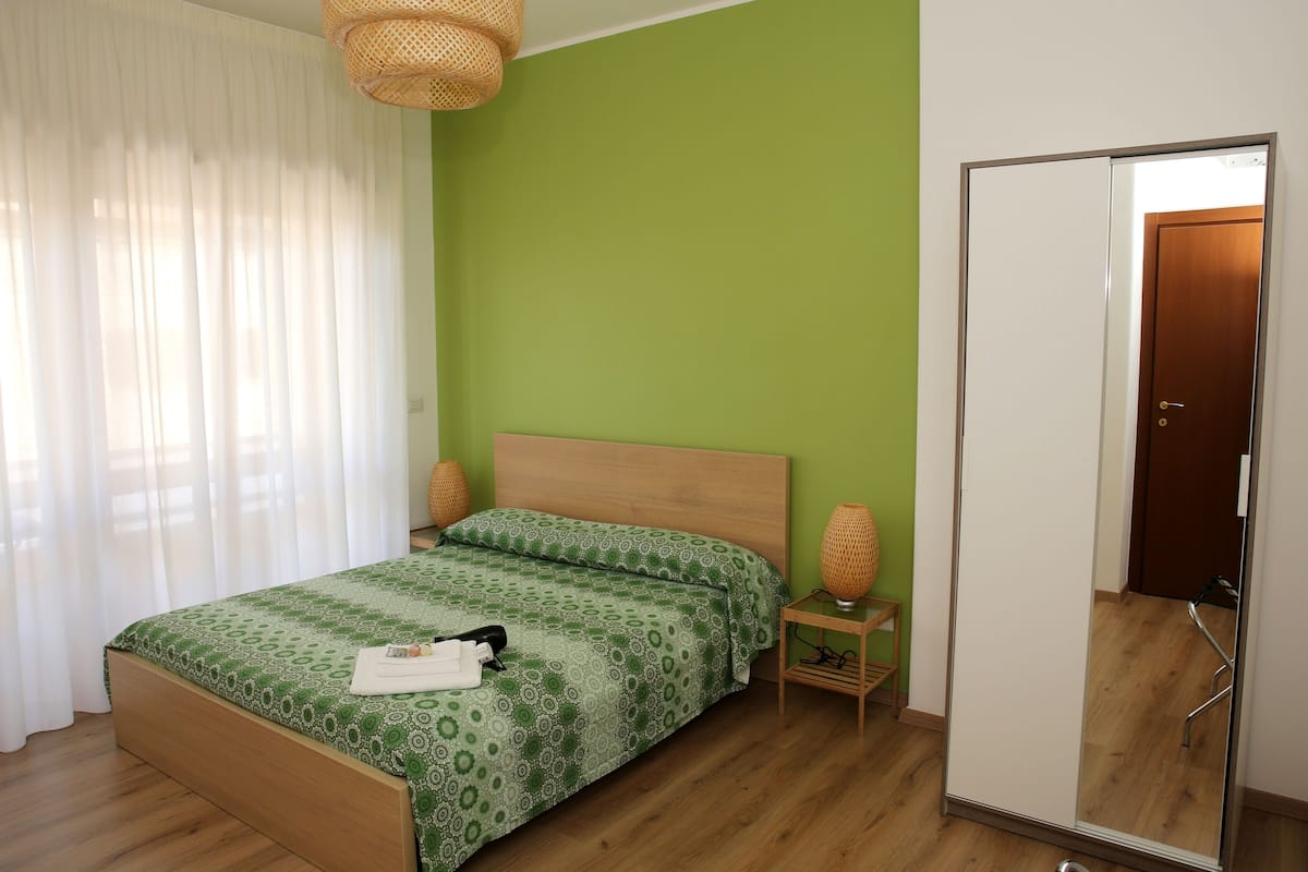 Una habitación con cama, armario, mesita de noche y ventana con cortinas.