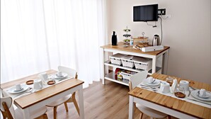 Un comedor con dos mesas de madera, sillas blancas y un carrito de buffet blanco con alimentos.