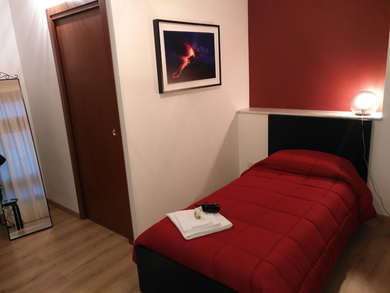 Une pièce avec un lit, une porte, un tableau encadré et une lampe de chevet.