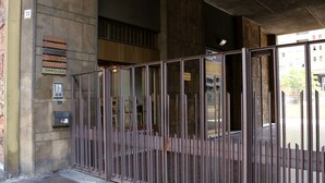 Una reja metálica con barras verticales, un cartel que dice "CENTRO DI CHIRURGIA" y la entrada de un edificio con un ventanal y una puerta.
