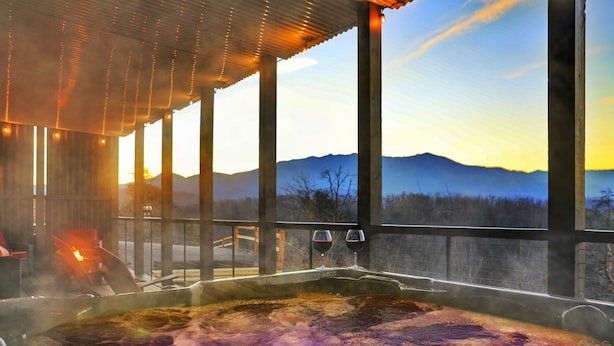A hot tub with a view of mountains, a wooden deck, and a sunset. - STUNNING Luxury Cabin! Game Room! 4 Fireplaces! Huge Decks Hot Tub! AMAZING View (Gatlinburg)