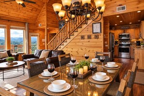 A wooden interior with a dining area set for a meal, a kitchen, and a staircase.