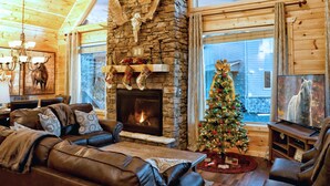 A cozy living room with a stone fireplace, leather sofa, and a Christmas tree. - STUNNING Luxury Cabin! Game Room! 4 Fireplaces! Huge Decks Hot Tub! AMAZING View (Gatlinburg)
