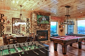 Une pièce chaleureuse équipée d’un baby-foot, d’une table de billard, d’une cheminée et d’un téléviseur fixé à un mur en pierre.
