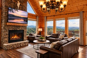 A cozy living room with a stone fireplace, leather sofas, and a large TV screen displaying a scenic view.