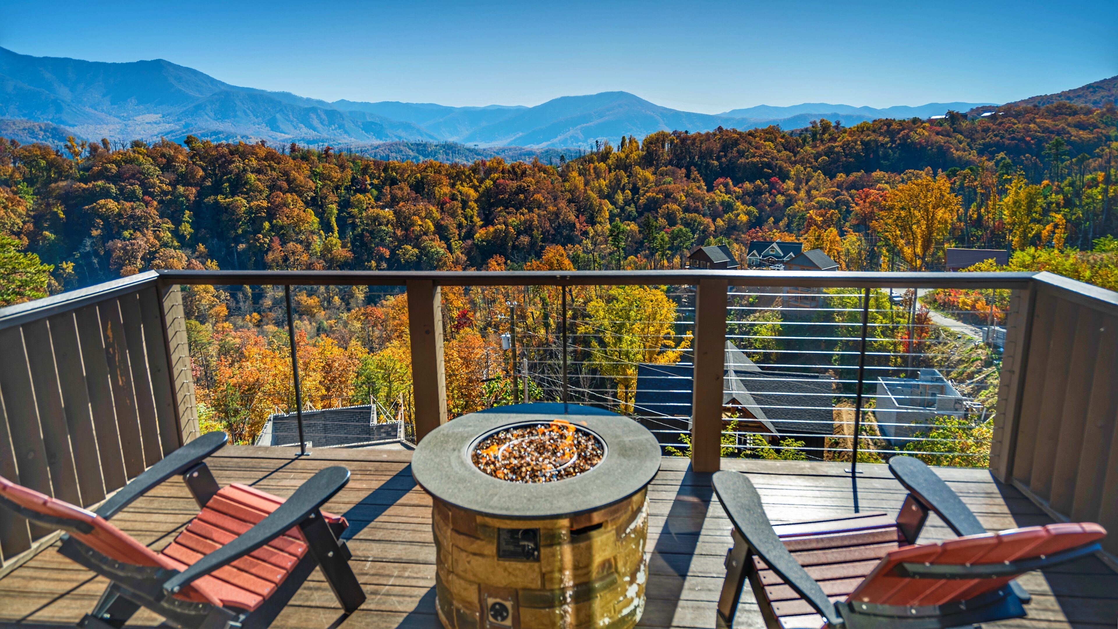 Eine Terrasse mit Feuerstelle, zwei roten Adirondack-Stühlen und Blick auf Herbstlaub und Berge.