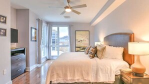 A bedroom with a bed, nightstands, a ceiling fan, a TV, and a window with curtains.