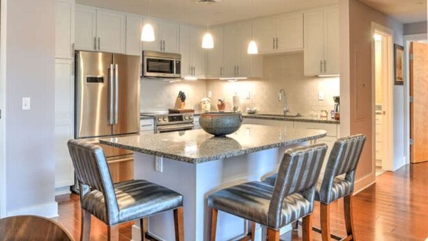 A modern kitchen with white cabinets, stainless steel appliances, and a central island with bar stools.