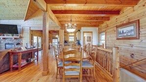 A wooden interior with a dining table surrounded by chairs, a kitchen area, and a television mounted on the wall. - Deck & Mtn Views! Luxe Log Cabin in Waynesville (Waynesville)