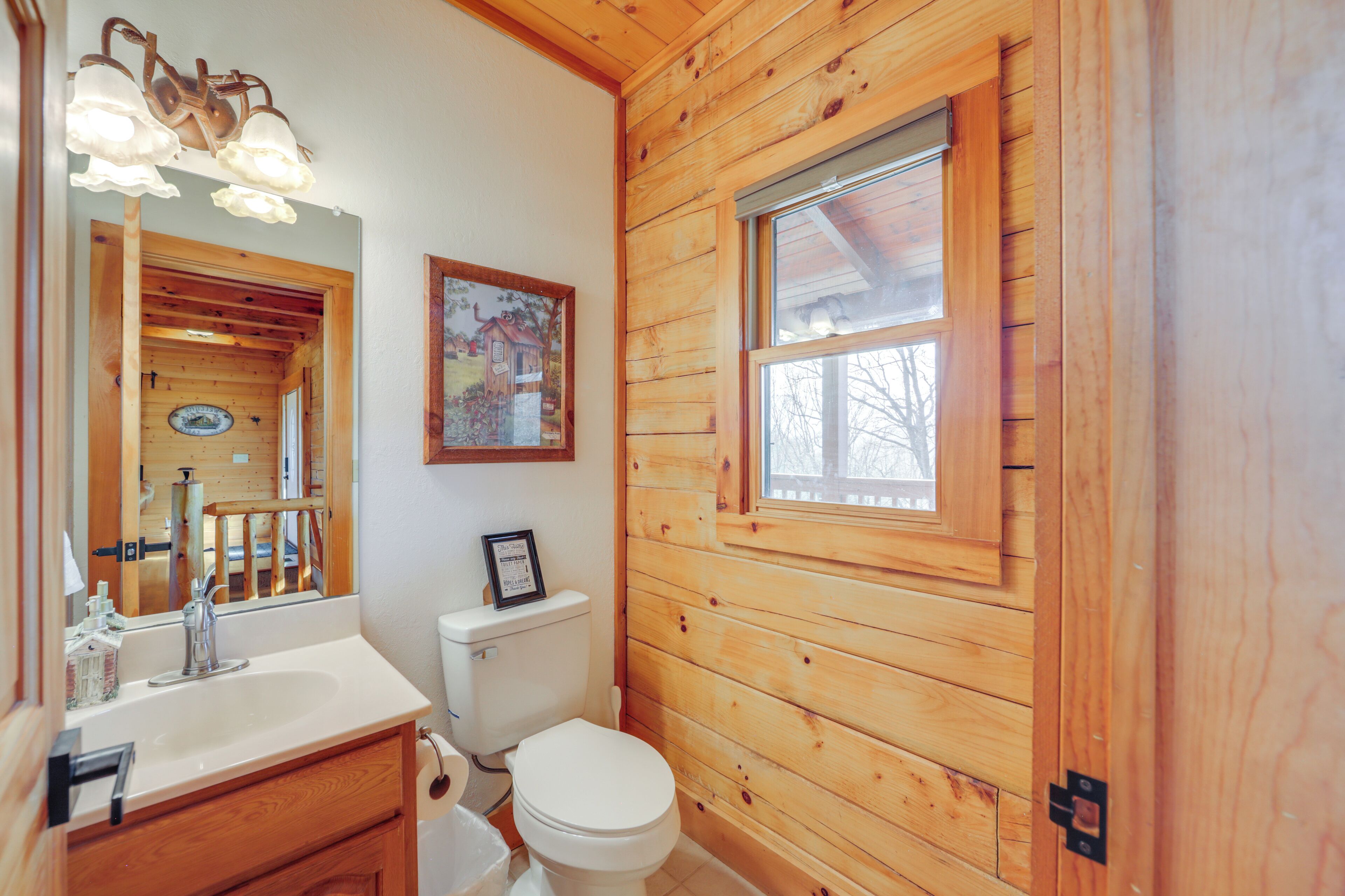 A wooden cabin bathroom with a sink, toilet, and a window.